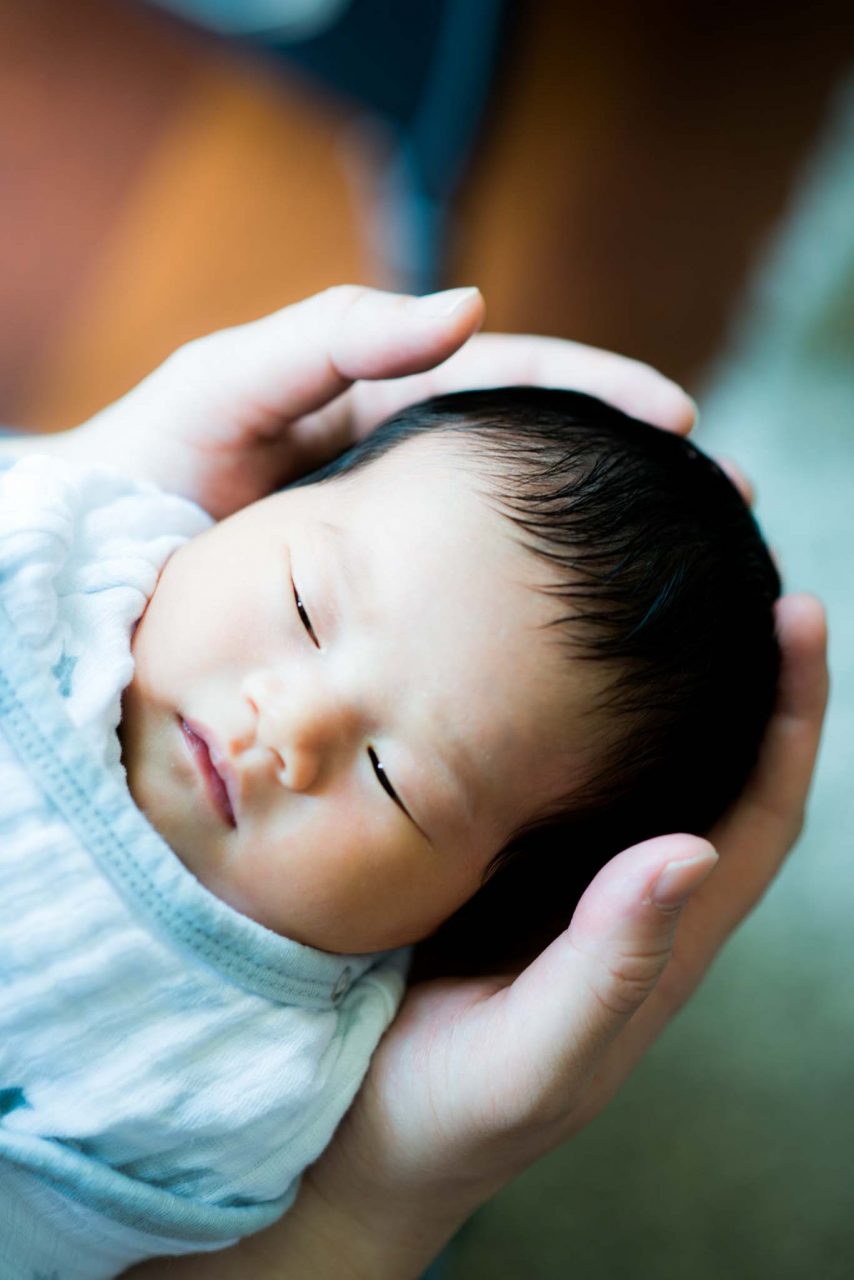 Sleeping newborn cradled in a parent’s hands