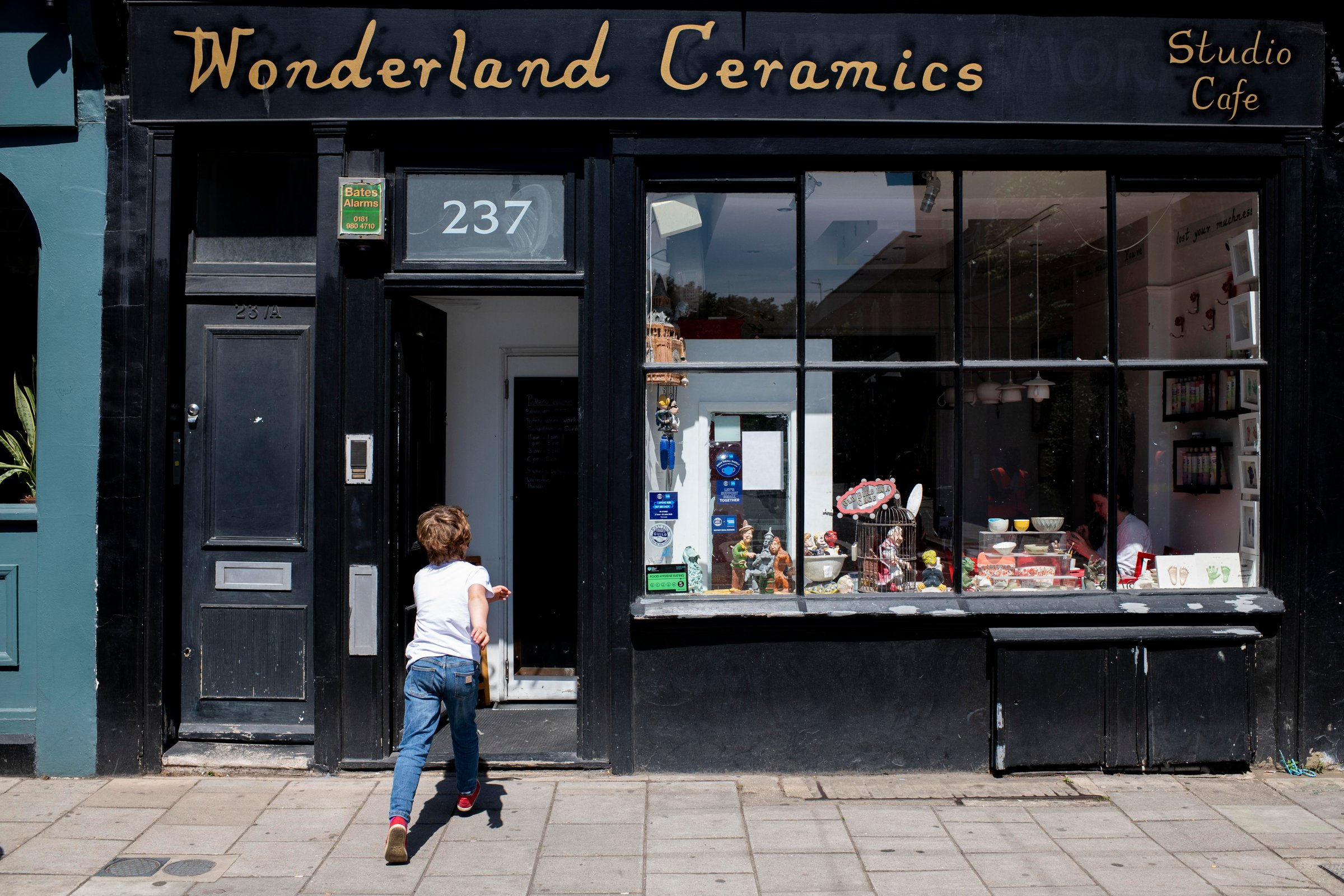 Child running into a ceramics café on a London street during a family photoshoot