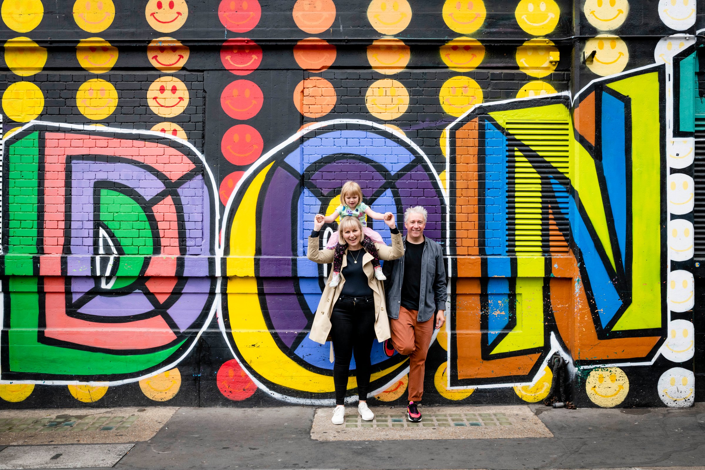 Family photoshoot in London, parents and toddler in front of a LONDON street-art mural