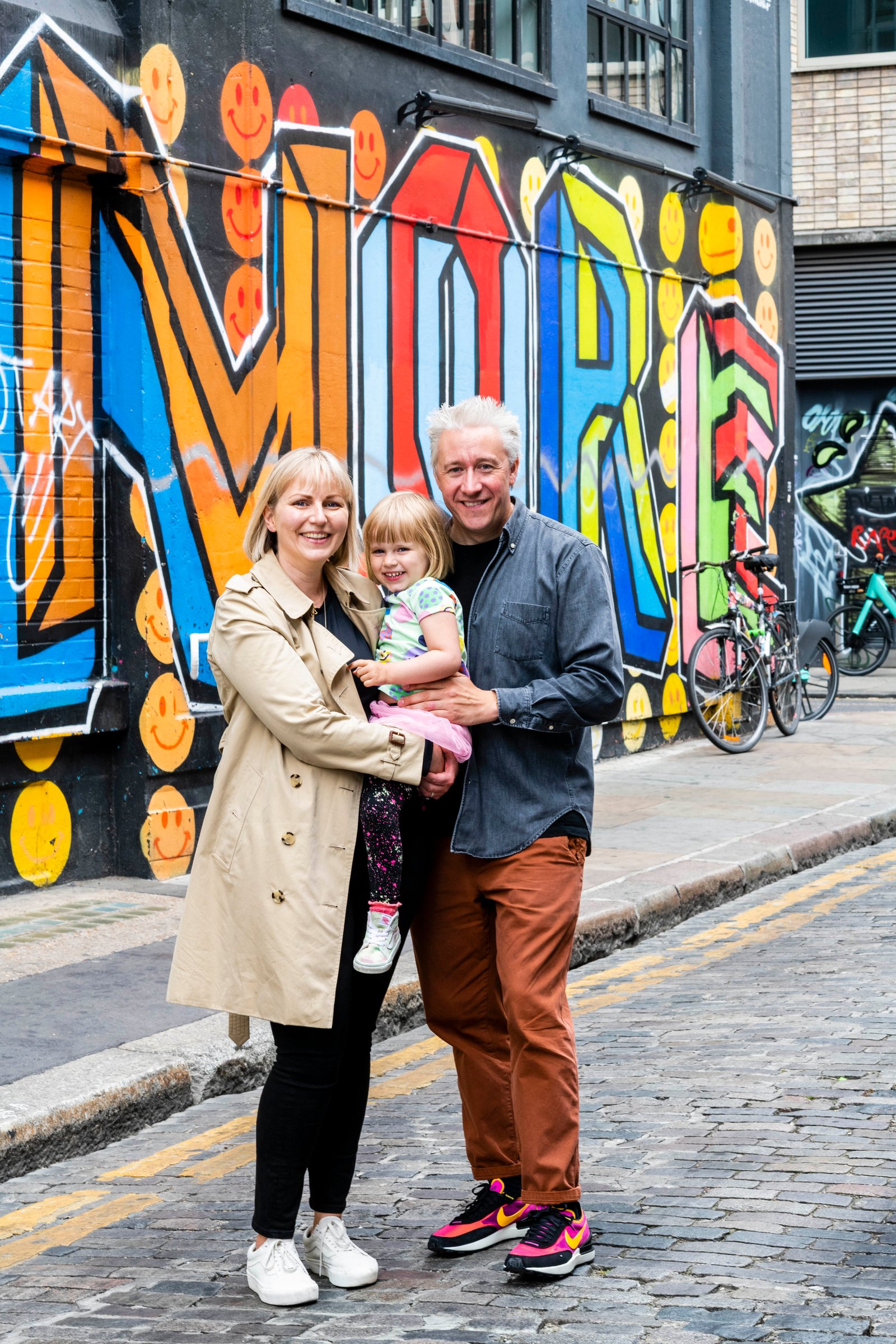 Parents holding their daughter on a cobbled London street lined with graffiti