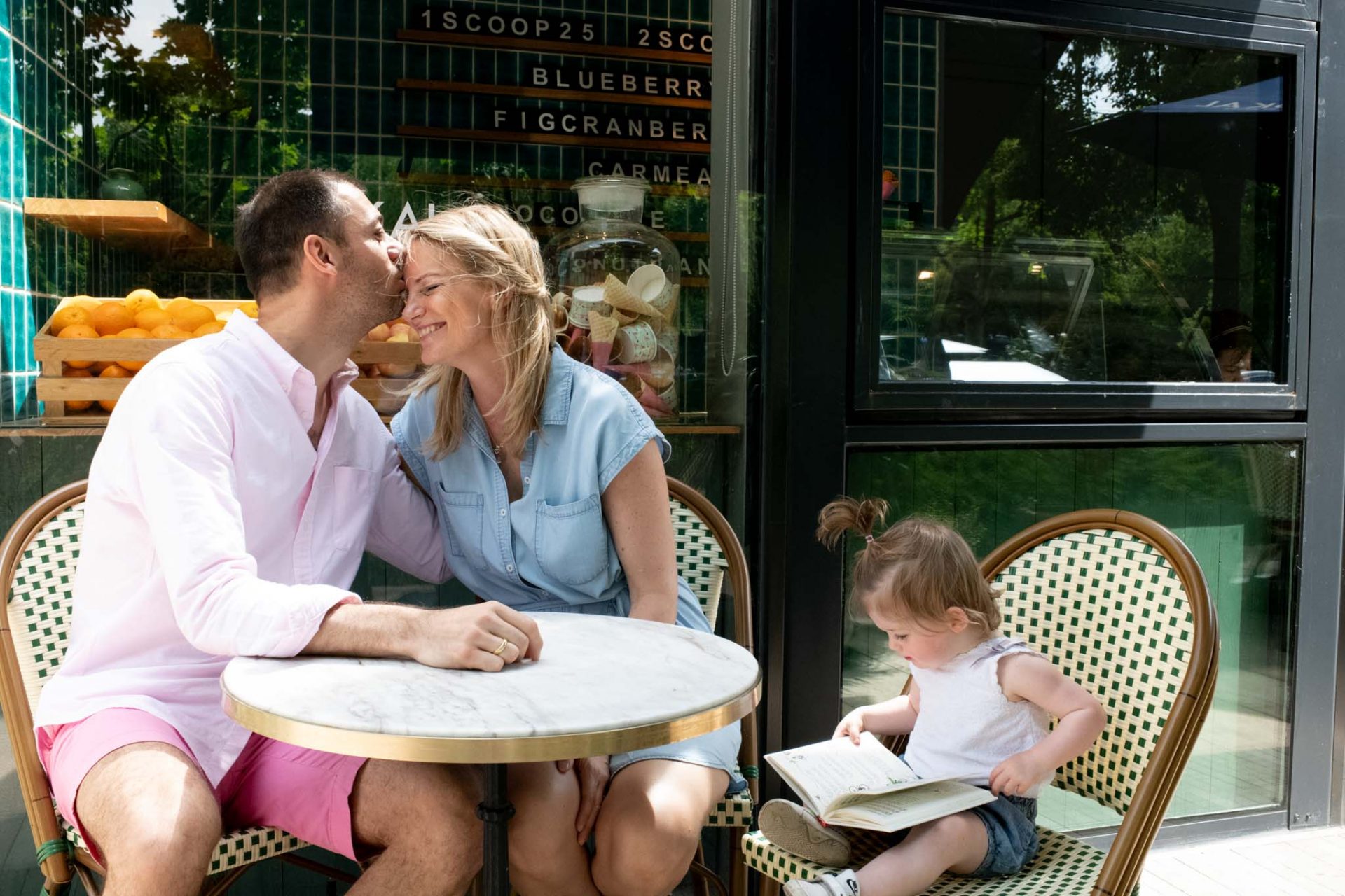 Family photoshoot at a café table, toddler reading a book